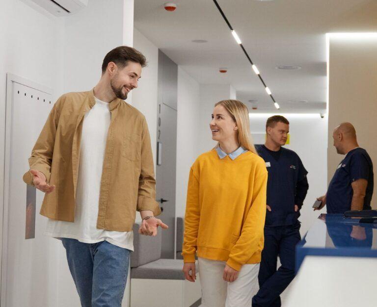 Банер до блогу для статті про підготовку до універсального чекапу: чоловік і жінка проходять повз рецепцію Файної Клініки і радісно щось обговорюють