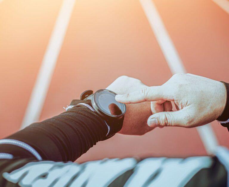 Банер до блогу до статті про відсутність результатів тренувань: чоловік дивиться на спортивний годинник на біговій доріжці на стадіоні