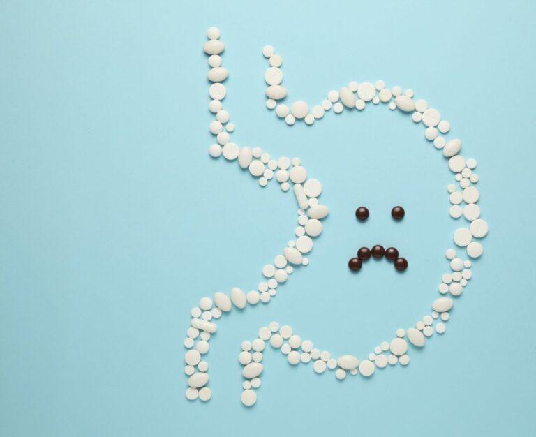 Банер для блогу для статті про гастрит: на блакитному фоні викладено білими таблетками форму шлунка і чорними таблетками йому викладено сумне обличчя