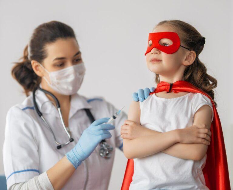 Банер до блогу до статті про вакцинацію від вітряної віспи: дівчинка в костюмі супергероя готується поки лікар їй зробить щеплення