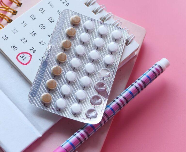Банер для блогу до статті про комбіновані оральні контрацептиви: на рожевому фоні лежить блокнот, ручка, календар і пластинка таблеток